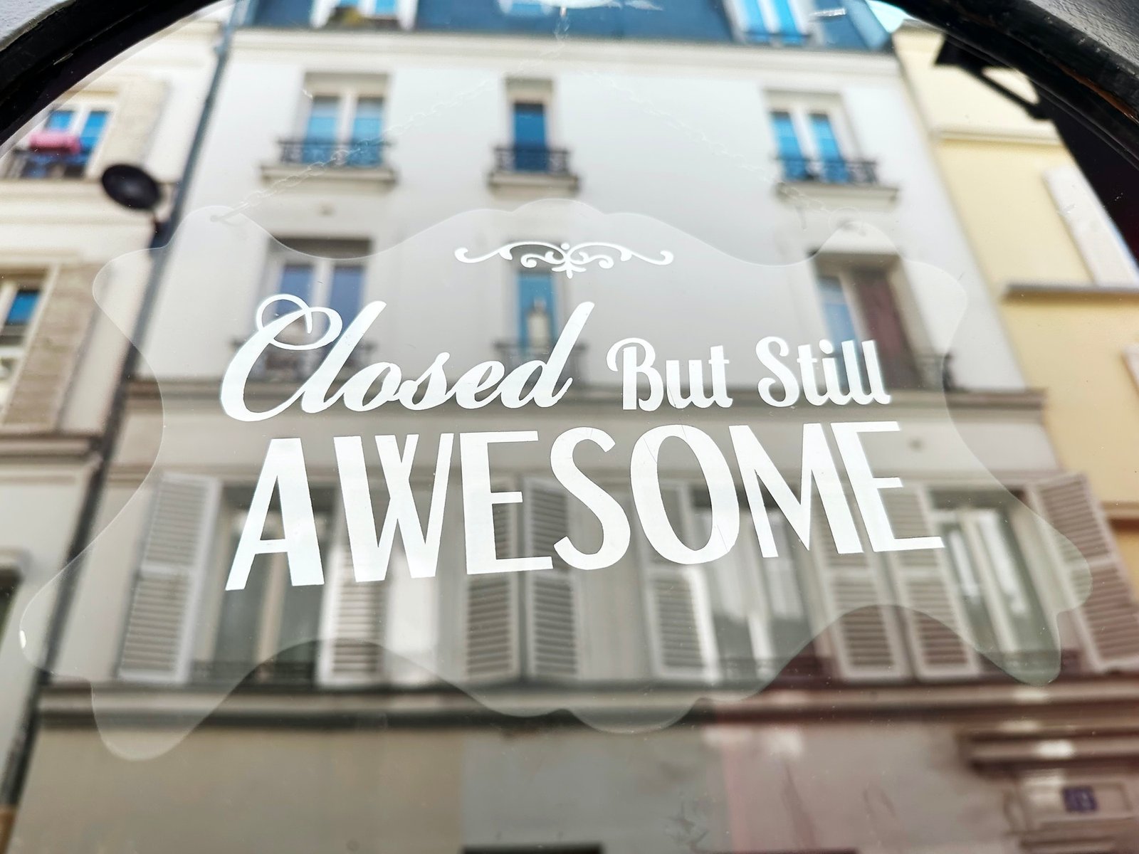 Phrase "Closed But Still Awesome" Written on Glass With Reflection of Local Architecture